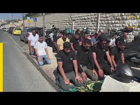 Muslims take part in Friday prayers as Israeli soldiers look on